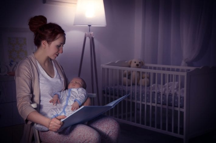 mother reading a book to her newborn baby at nighttime keeping calm