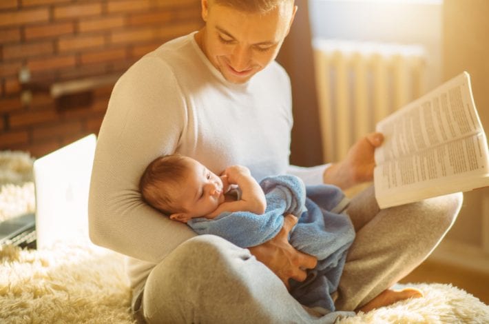 Dad and baby - dad reading book to baby and smiling. Dad and baby bonding