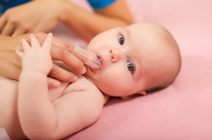 baby with mother scratching gums iwth finger and toothbrush