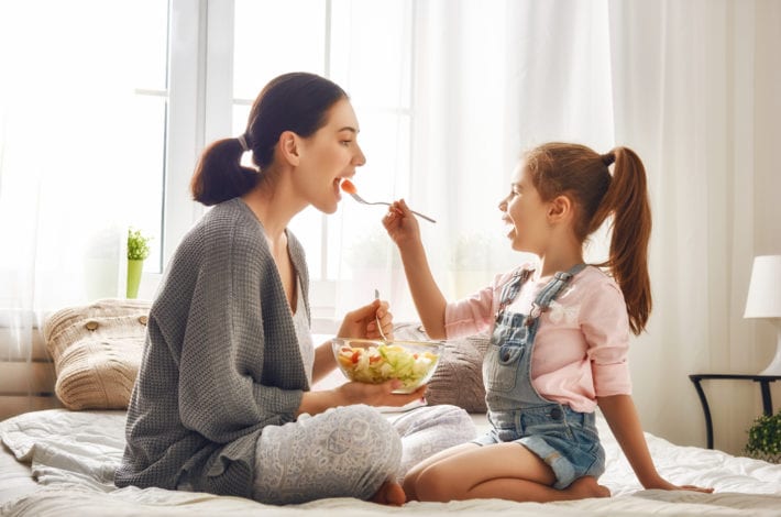mother eating healthily - fed fruit salad by daughter