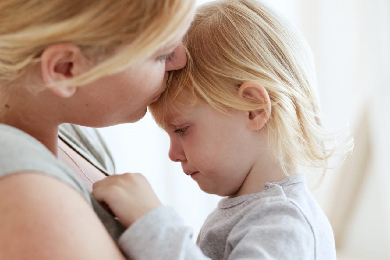 mother kissing crying toddler on forehead - managing terrible twos