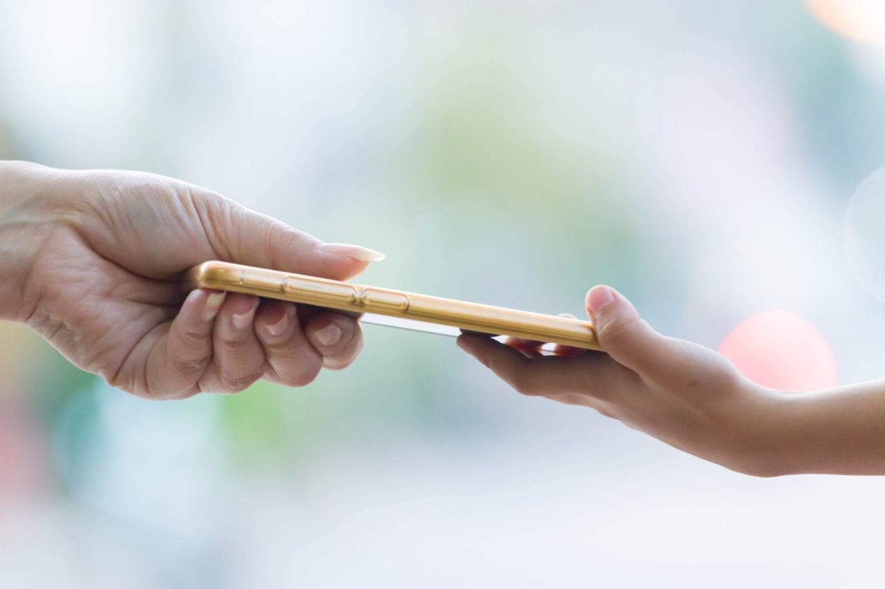  A close-up image of a parent and child holding a smartphone together.