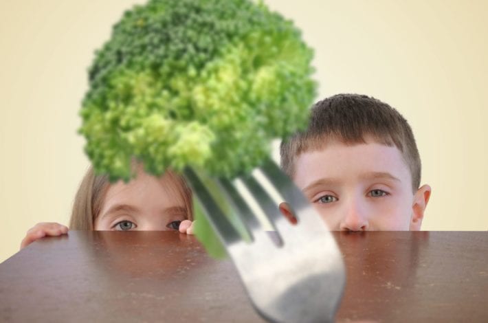 two children looking at a piece of broccoli suspiciously