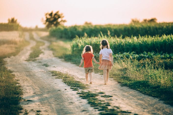 two sisters walking down a path together holding hands