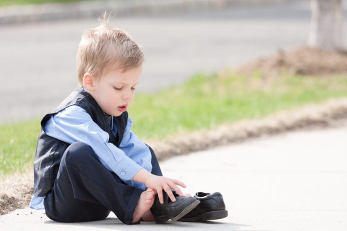 young boy trying to put on his shoes